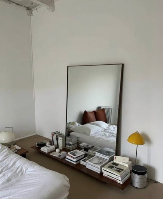 Chambre claire, miroir posé contre le mur et pile de livres sur une table de chevet