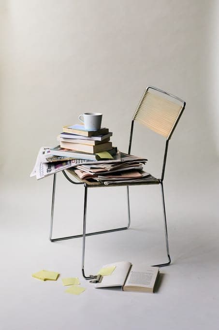 Chaise en métal chargée de livres et de papiers, sur fond clair